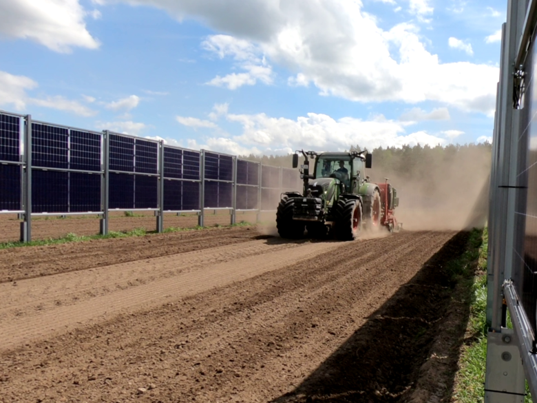 Traktor fährt zwischen den Modulreihen einer Agri-PV Anlage