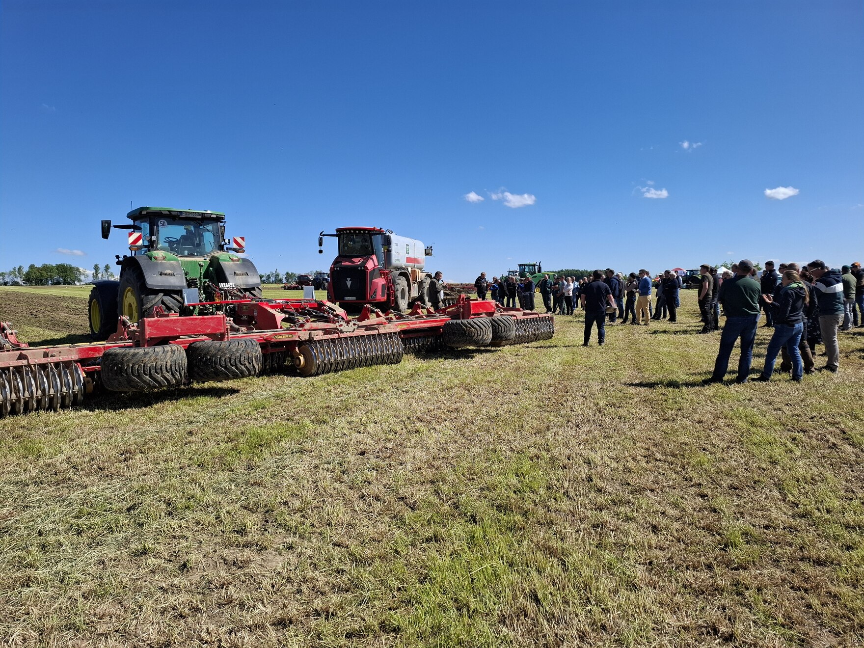 Verschiedene Landmaschinen und eine Personengruppe auf einem Feld