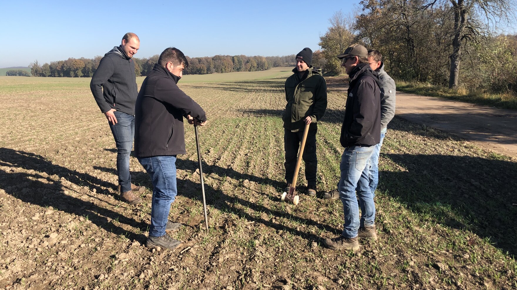 Fünf Personen stehen mit einem Bohrstock auf einem Feld.