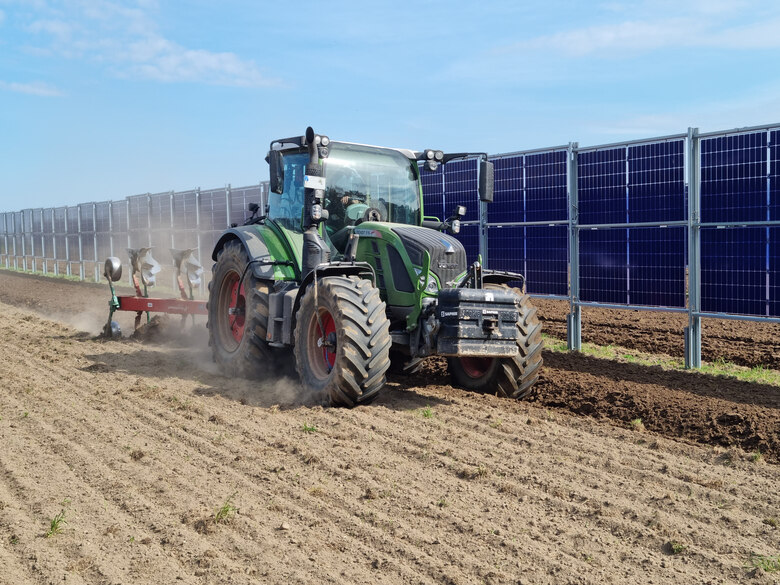 Traktor mit Pflug vor einer vertikalen Agri-PV Anlage auf dem Feld