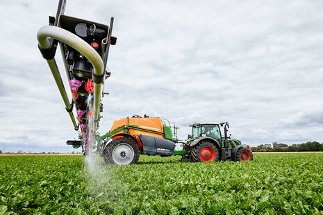 Traktor mit Spritze fährt über das Feld und versprüht Pflanzenschutzmittel. 